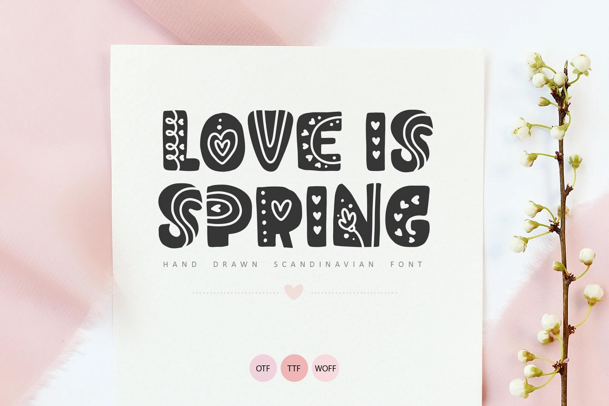 Decorative text saying "Love is Spring" in a hand-drawn Scandinavian font. Accompanied by a floral branch and a pink fabric background.