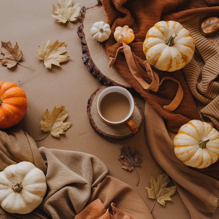 Autumn-themed flat lay featuring pumpkins, fall leaves, cozy sweaters, and a cup of coffee on a wooden coaster, evoking a warm, seasonal atmosphere.