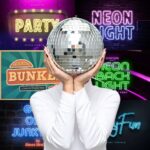 A person holds a disco ball, surrounded by colorful neon signs displaying various typography styles and vibrant party-themed designs.